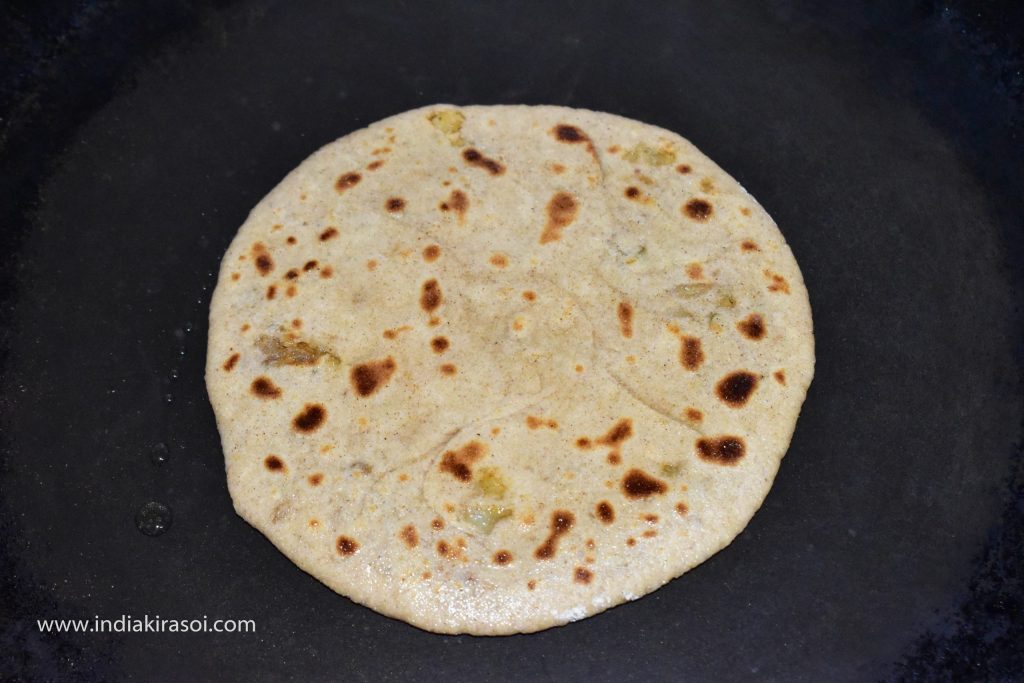 Take one teaspoon of oil or desi ghee in a spoon and spread it on the paratha. Apply oil or desi ghee on the whole surface of the paratha.