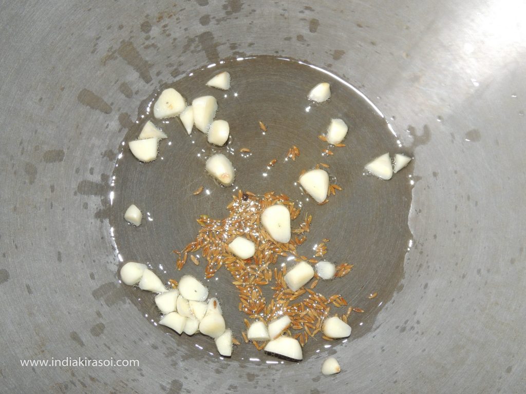 When the cumin starts crackling, add chopped garlic.