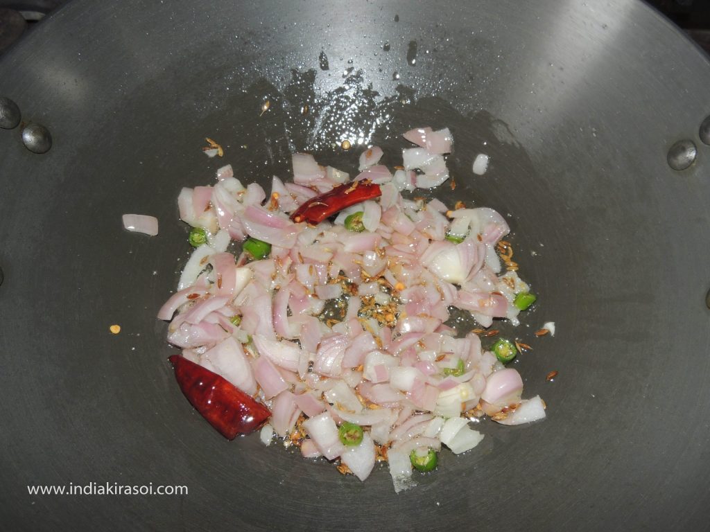 After this, add chopped onion and chopped green chilies in the kadhai/ fry pan.