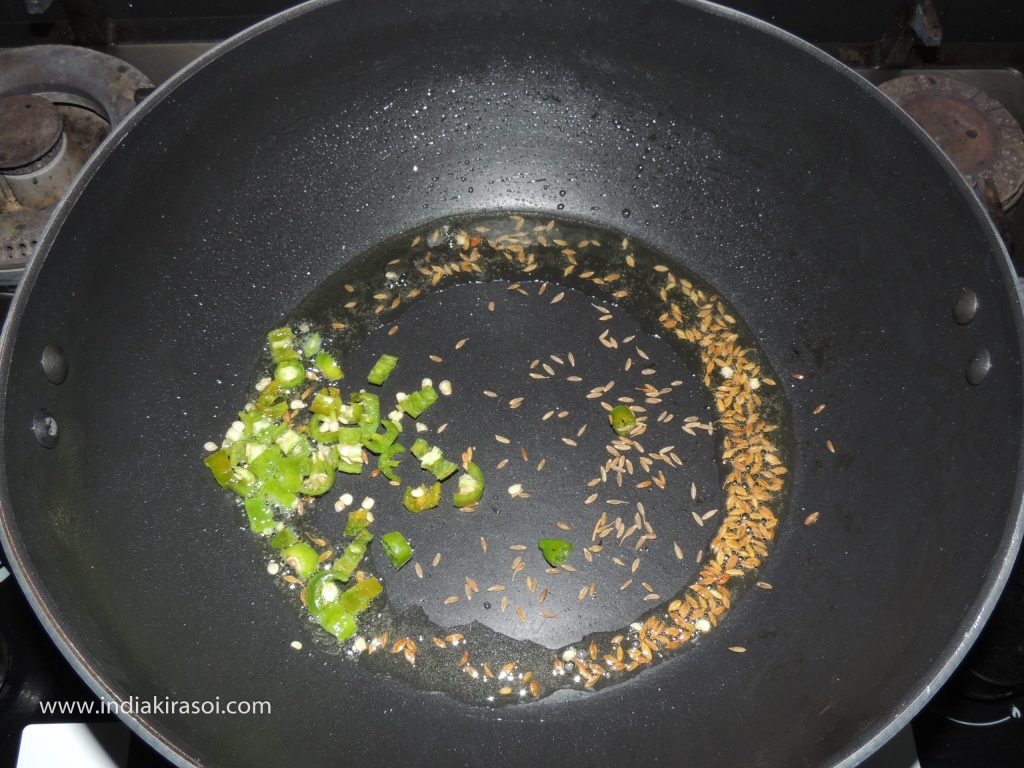 When the cumin starts crackling, add chopped green chilies to the oil.