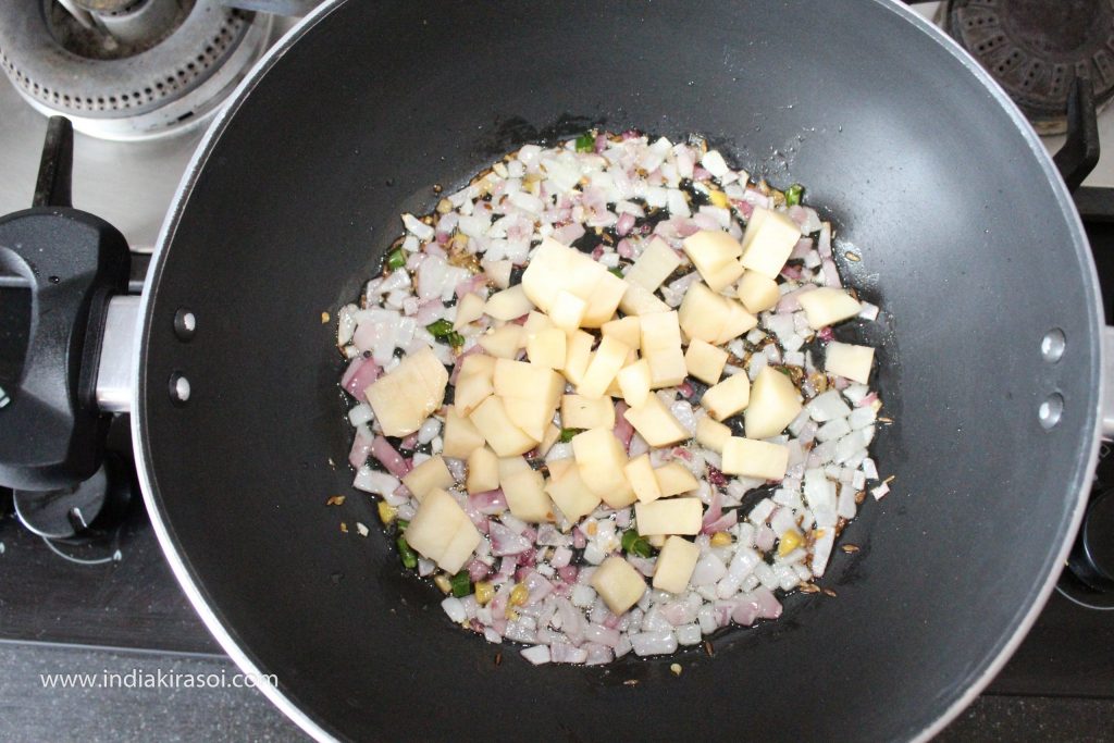 When the onions turn light pink, add chopped potatoes to the kadhai/ fry pan.