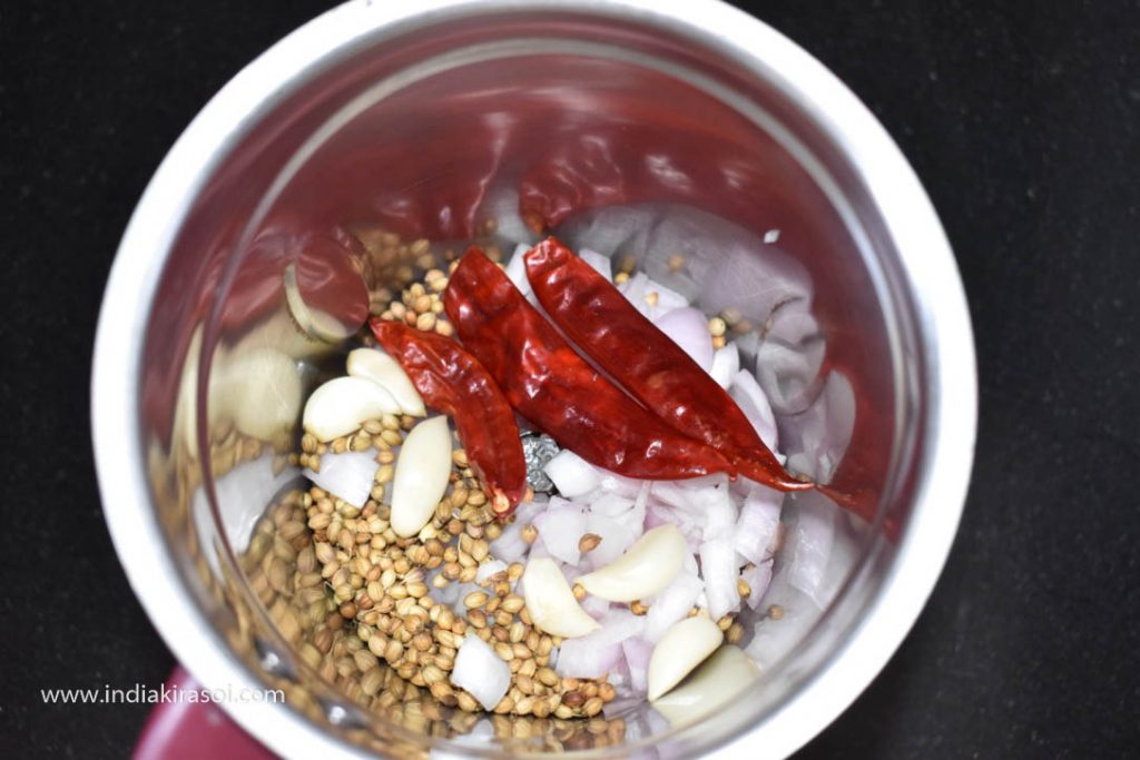 Now add coriander seeds, chopped onions, garlic, whole red chilies, garlic to the jar of the mixer grinder.